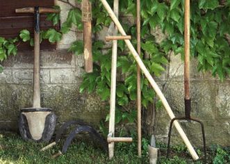 Bäuerliche Arbeitsgeräte, wie Sense oder Spaten, vor mit wildem Wein bewachsenem Gebäude